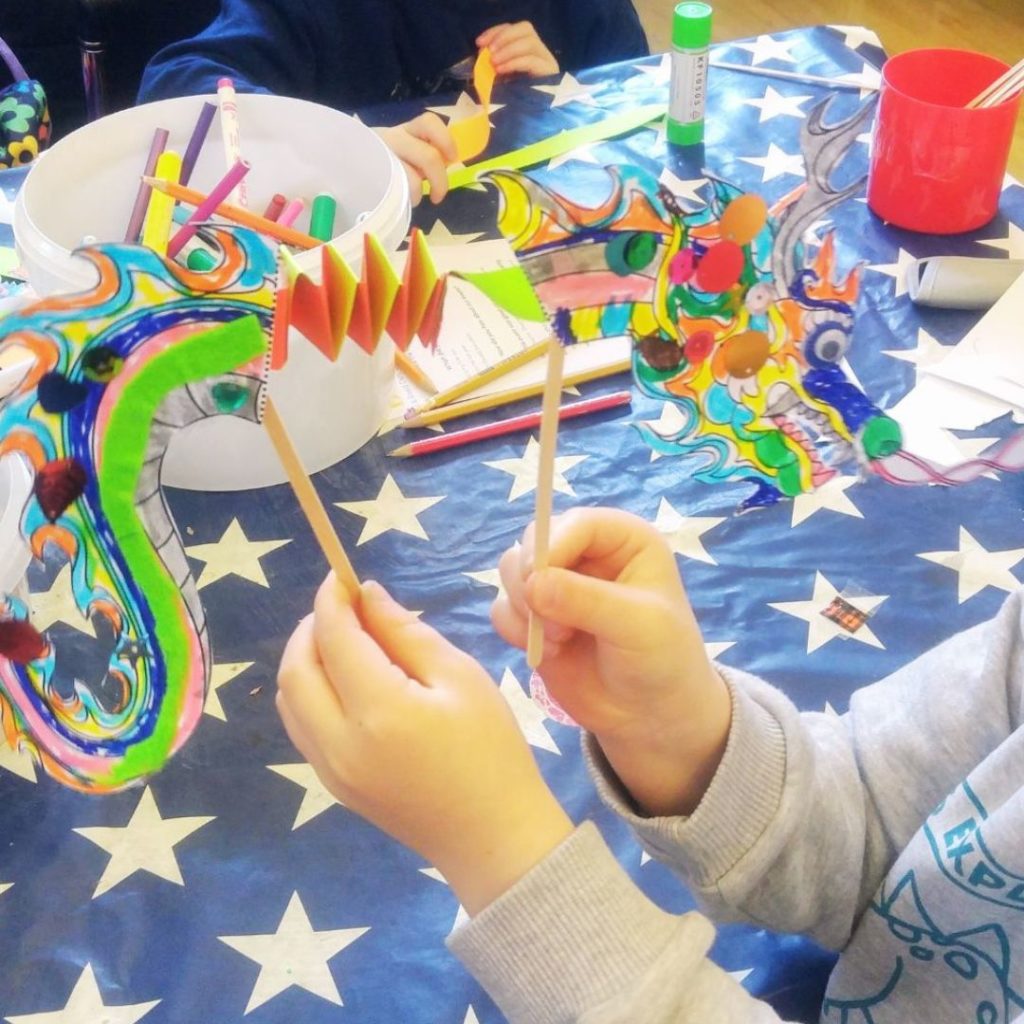 A child's hands holding a paper dragon puppet.